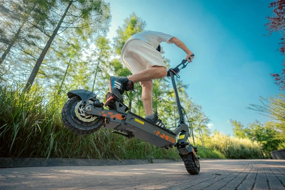 Förare hoppar med en svart KuKirin-elsparkcykel med orange detaljer upp från en trottoar – KuKirin G2 Pro vs G4 vs G2 Master