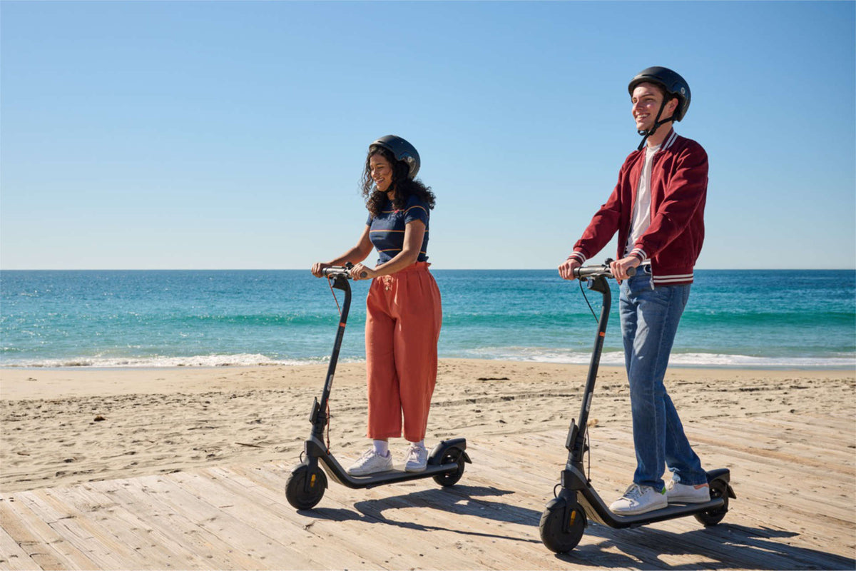 Två förare med hjälm på elsparkcyklar på en träbrygga vid havet – regler för elsparkcykel