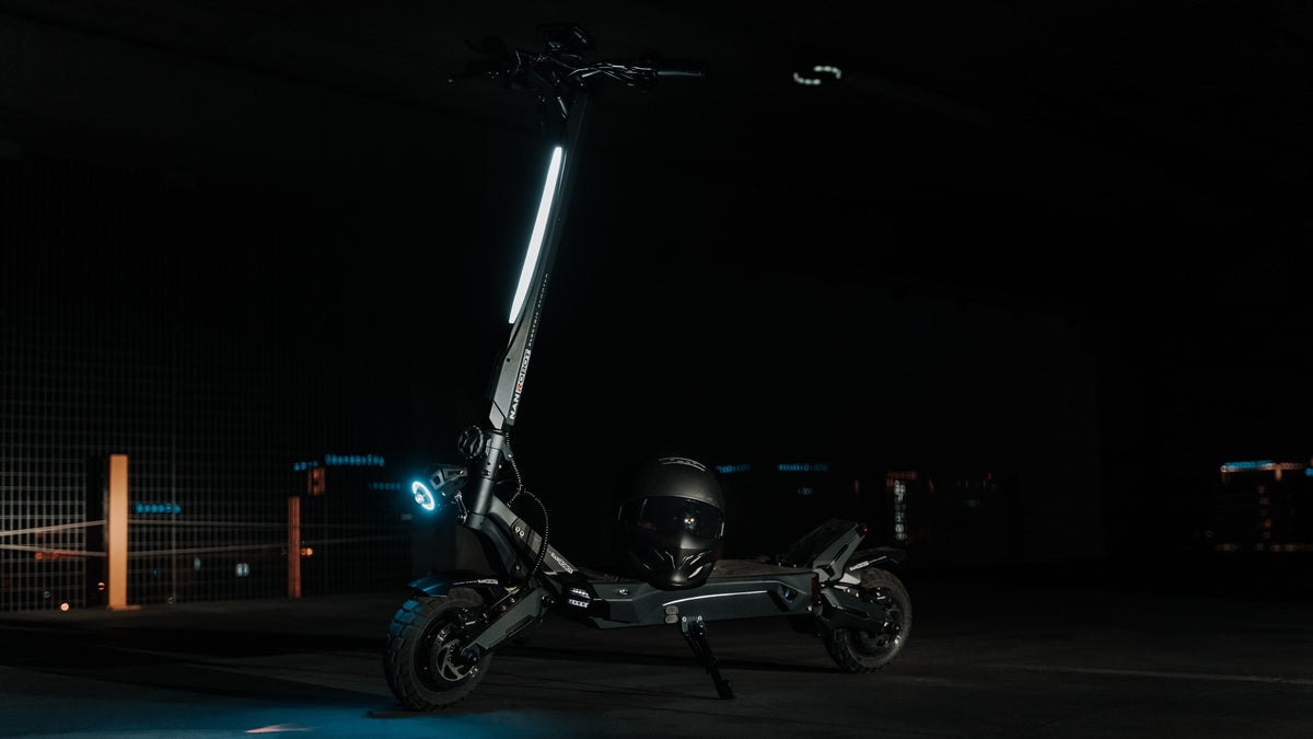 Svart elsparkcykel parkerad på stödbenet i ett mörkt garage, med en hjälm på fotplattan