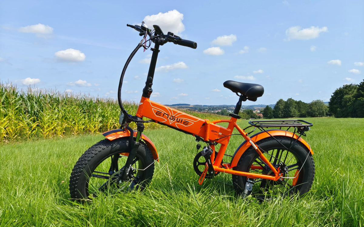 Orange hopfällbar ENGWE EP-2 Pro elcykel med breda däck och pakethållare i högt gräs vid ett majsfält under blå himmel