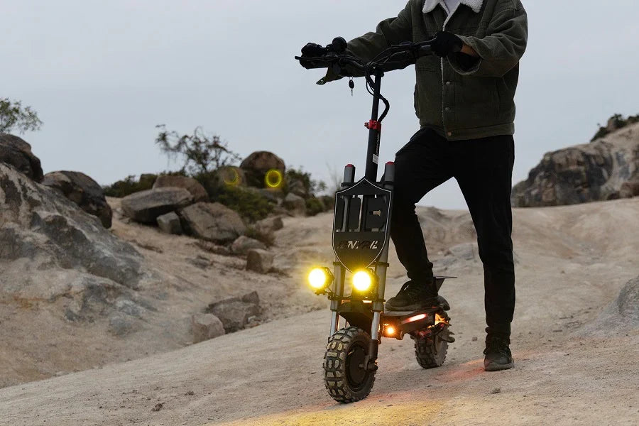 Elsparkcykel med tända framlampor i skymningen på en klippig terrängstig
