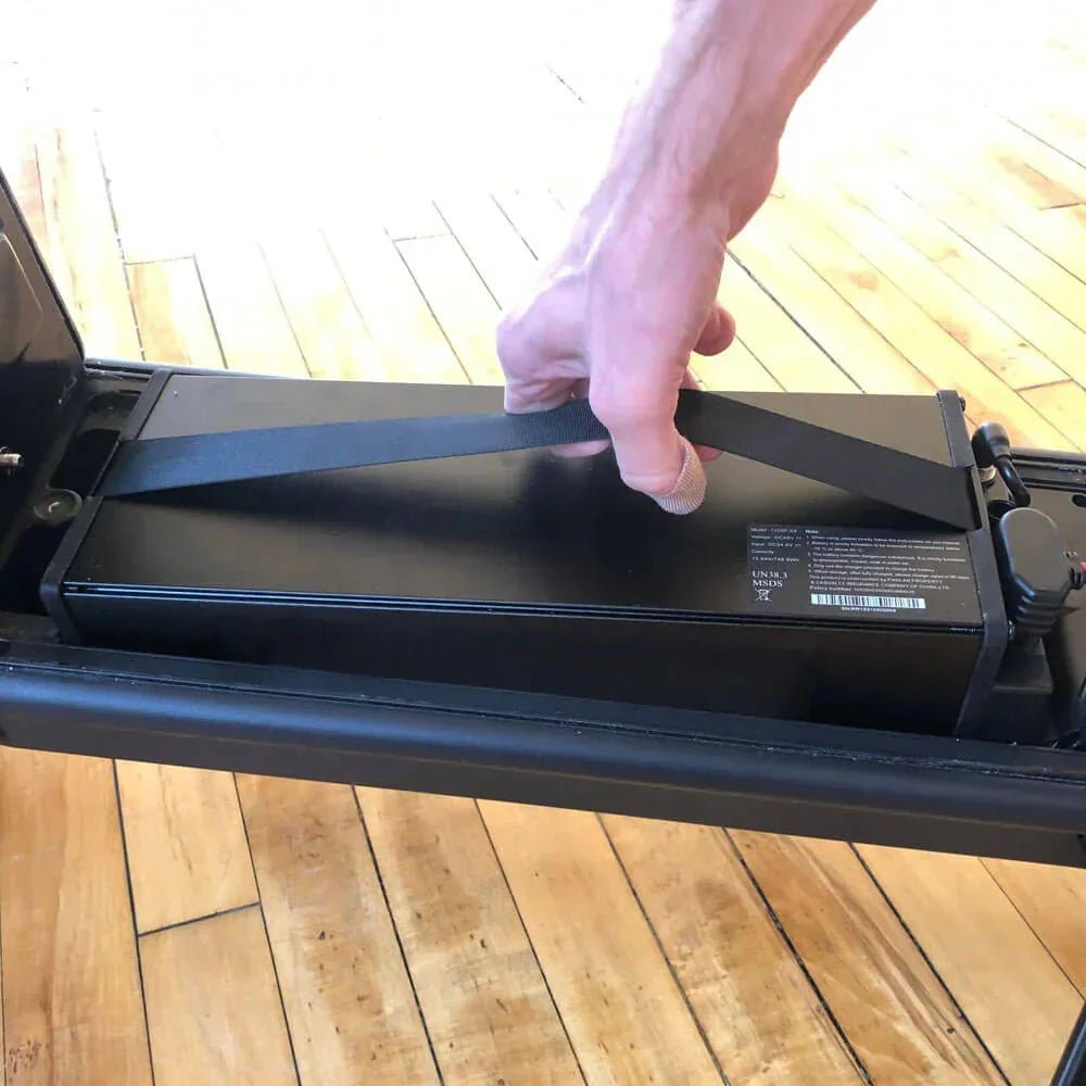 Hand lyfter ut elsparkcykelns löstagbara batteri i bärremmen, inomhus – ett batteri laddas bäst i rumstemperatur