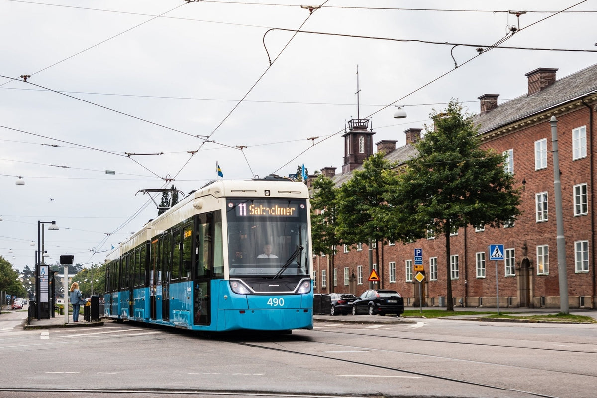 Blå och vit spårvagn på linje 11 mot Saltholmen på en gata i Göteborg, bredvid en hållplats och en tegelbyggnad