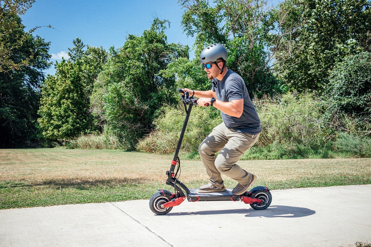 Man med hjälm och solglasögon kör en kraftig elsparkcykel med fjädring på en betongväg i en park – för- och nackdelar
