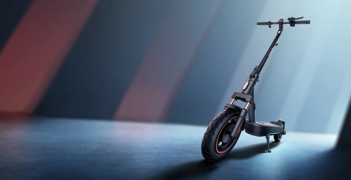 Svart Xiaomi-elsparkcykel med fjädrad framgaffel och grovt luftdäck står på stödbenet i en studio med rött och blått ljus