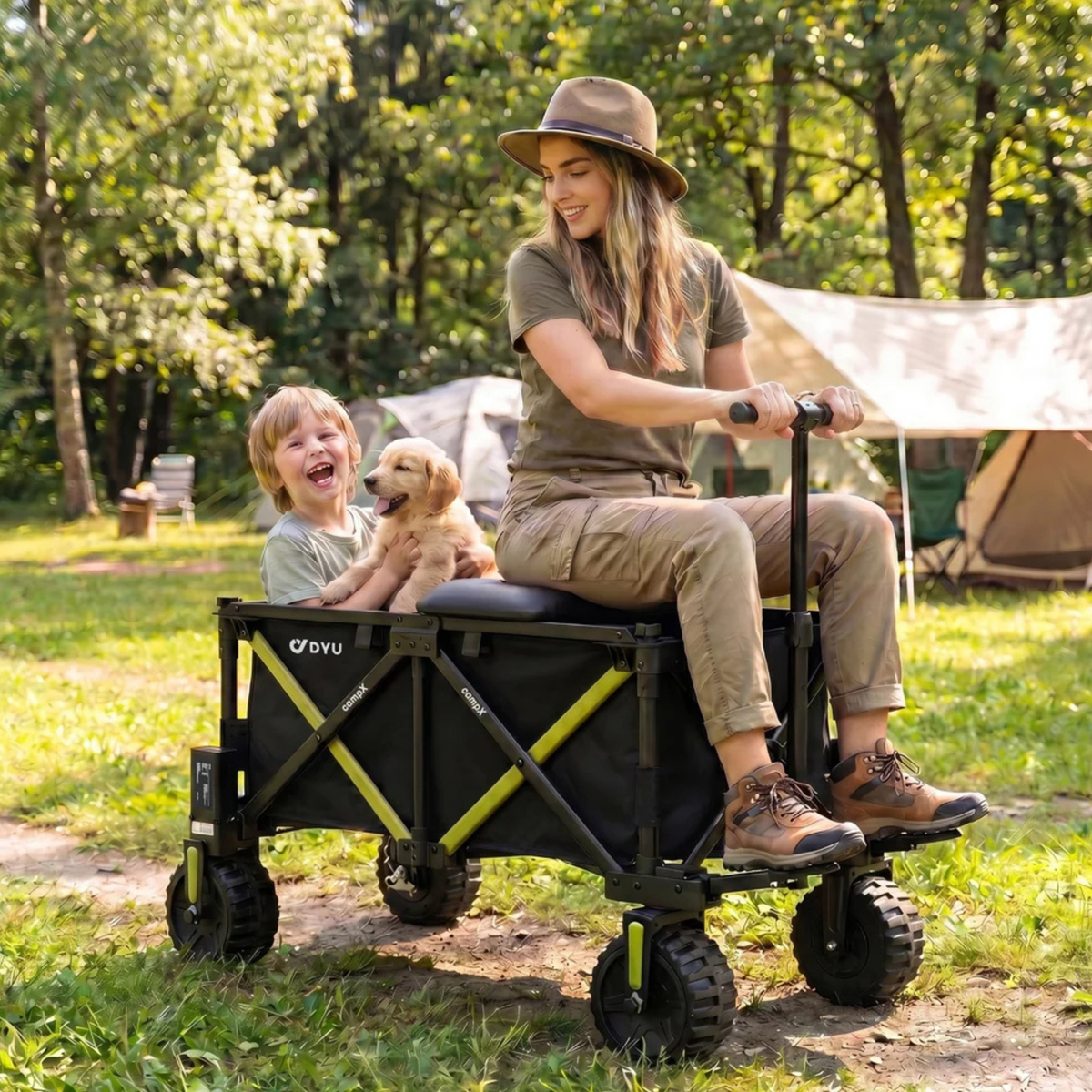 DYU Campx på gräs vid tält, en kvinna sitter på vagnen och ett barn med en valp sitter i vagnen