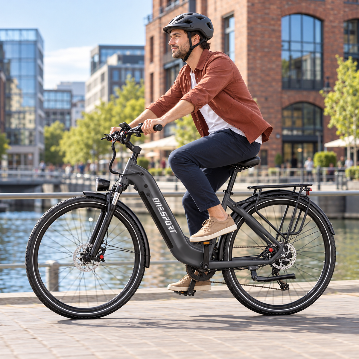 Man med hjälm cyklar en mörkgrå OneSport OT05 Max längs en kaj vid vattnet