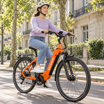 Kvinna med hjälm cyklar en orange OneSport OT05 Max på en gata med träd och fasader