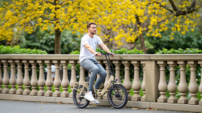 Man i vit t-shirt cyklar beige OneSport OT16 Pro förbi stenbalustrad och gula blommande träd