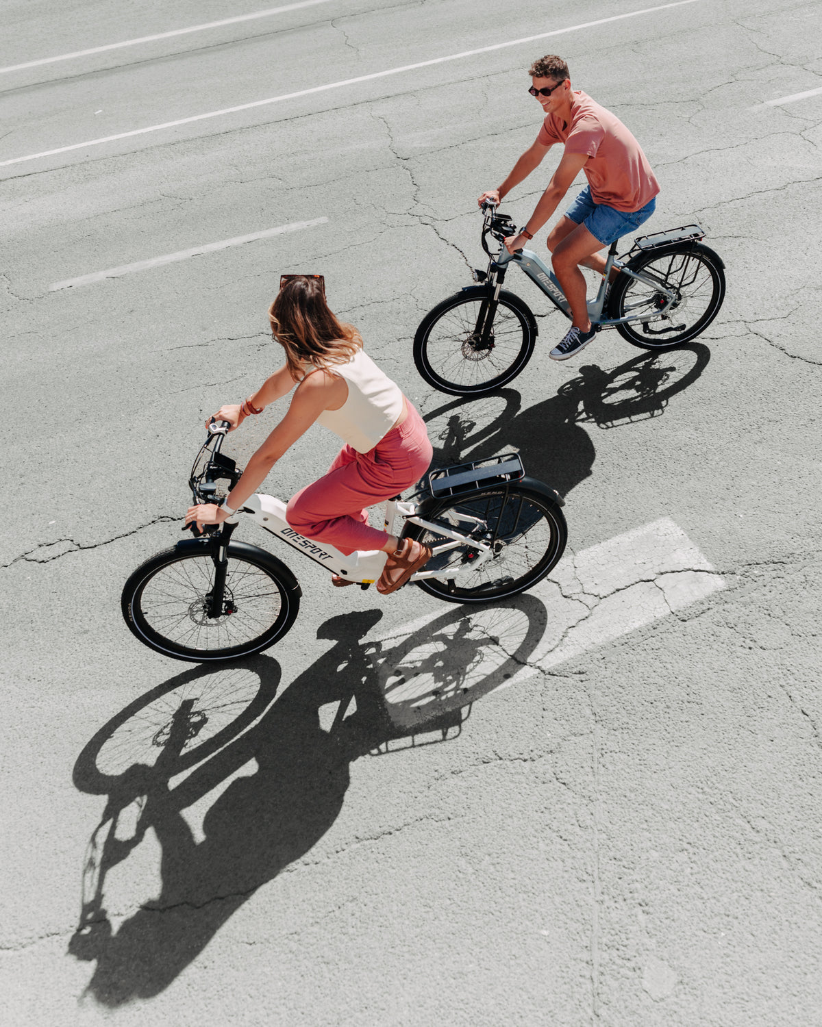 OneSport WT05 sedd ovanifrån, kvinna på vit cykel och man på grå cykel cyklar på asfalt med skuggor