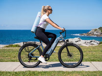 OneSport WT05 i sidovy, kvinna med yogamatta på ryggen cyklar längs havet