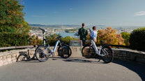 Två OneSport WT05 parkerade vid ett stenräcke på en utsiktsplats med två personer och utsikt över stad och flod