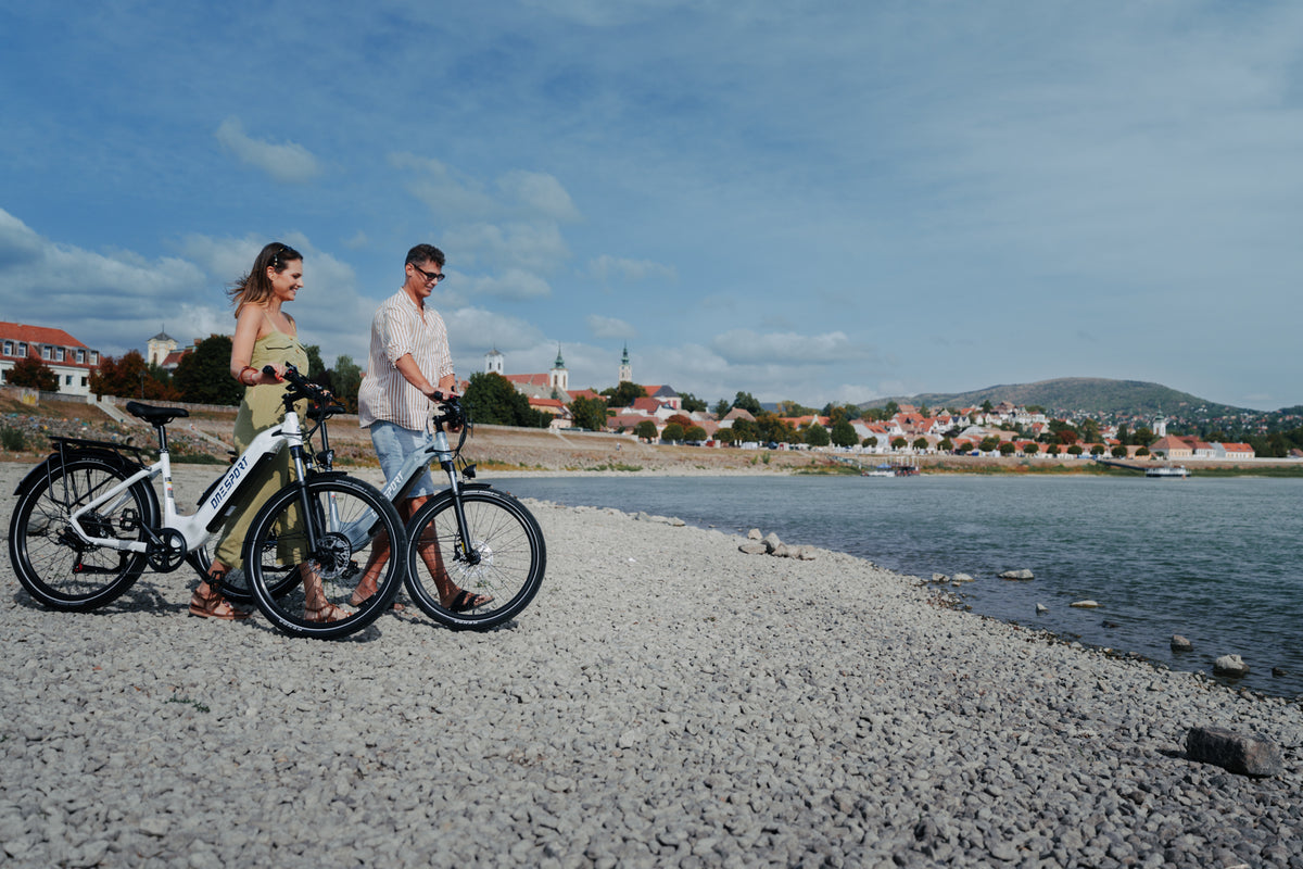 Två personer leder varsin OneSport WT05 längs en stenstrand med stad och kulle i bakgrunden