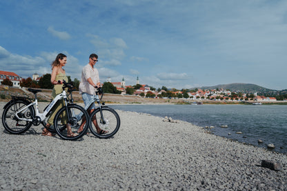 Två personer leder varsin OneSport WT05 längs en stenstrand med stad och kulle i bakgrunden