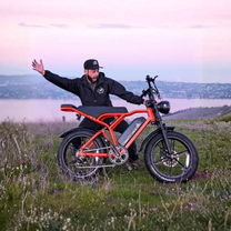 Man står med TST R002 Plus fatbike-elcykel i färgen orange på en gräsplan