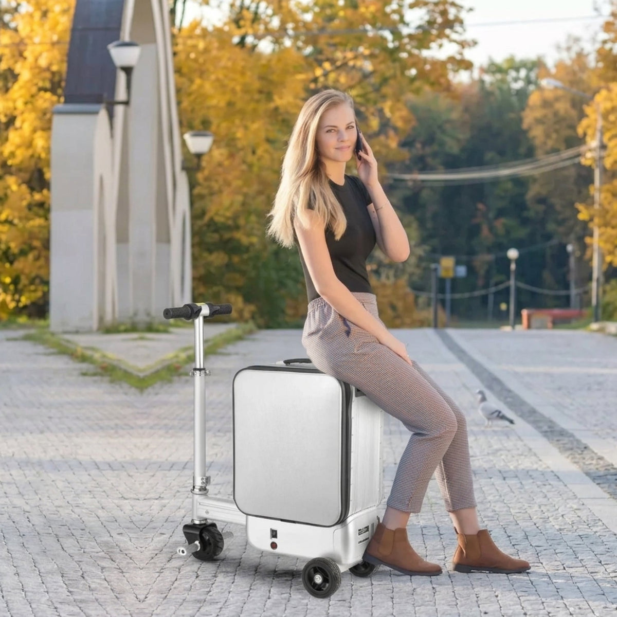 Person sitter på AeroDrive Edition elektrisk åkbar resväska i höstmiljö