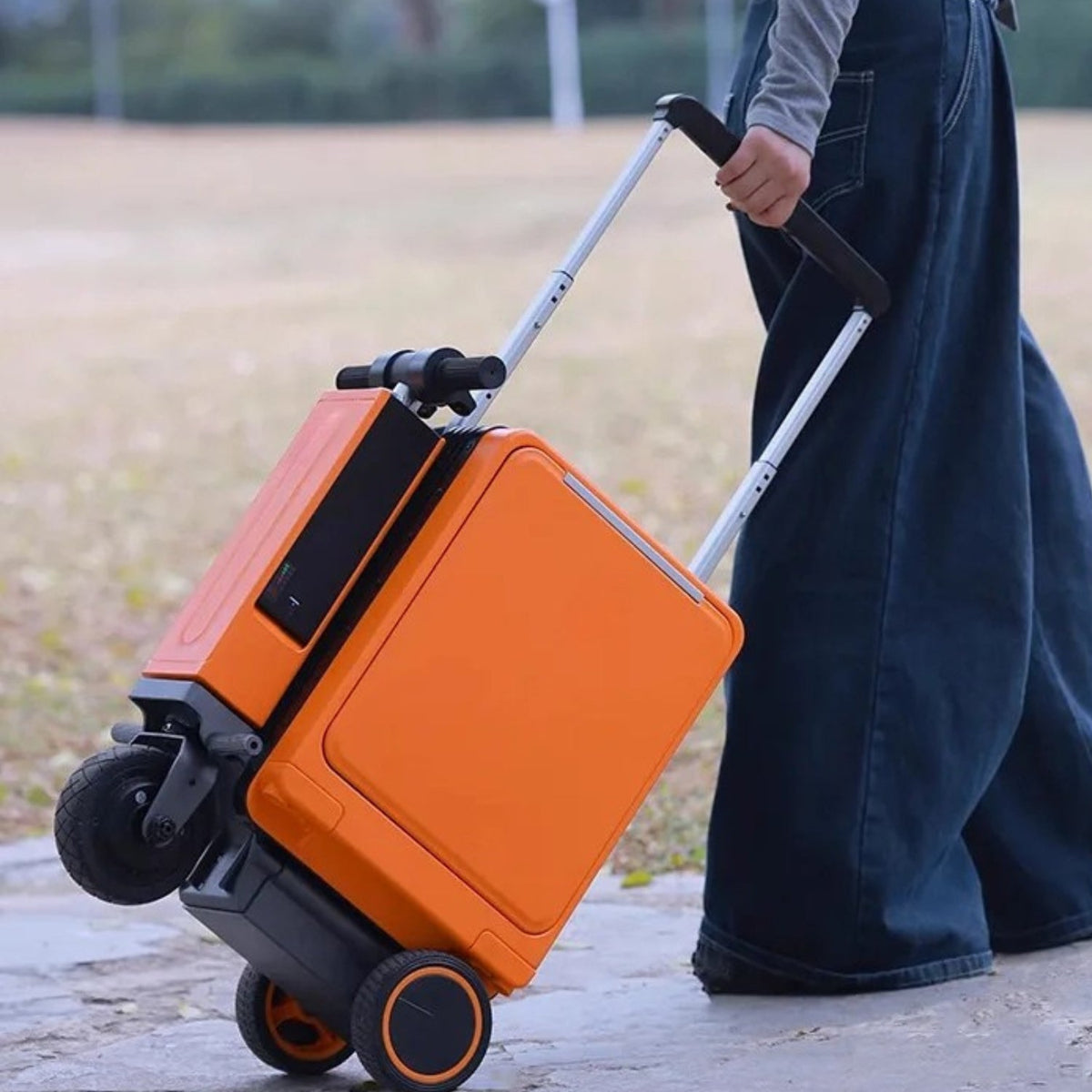 Person drar Urban Move Edition elektrisk åkbar resväska i orange utomhus