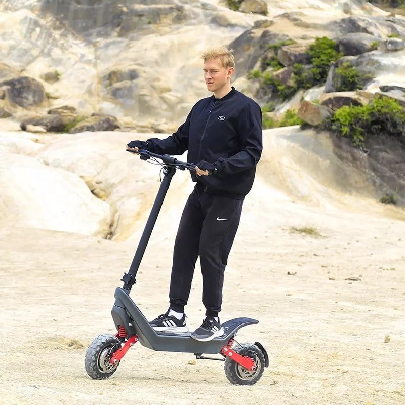 Man står med HX X10 elsparkcykel i sandig terräng