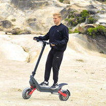Man står med HX X10 elsparkcykel i sandig terräng