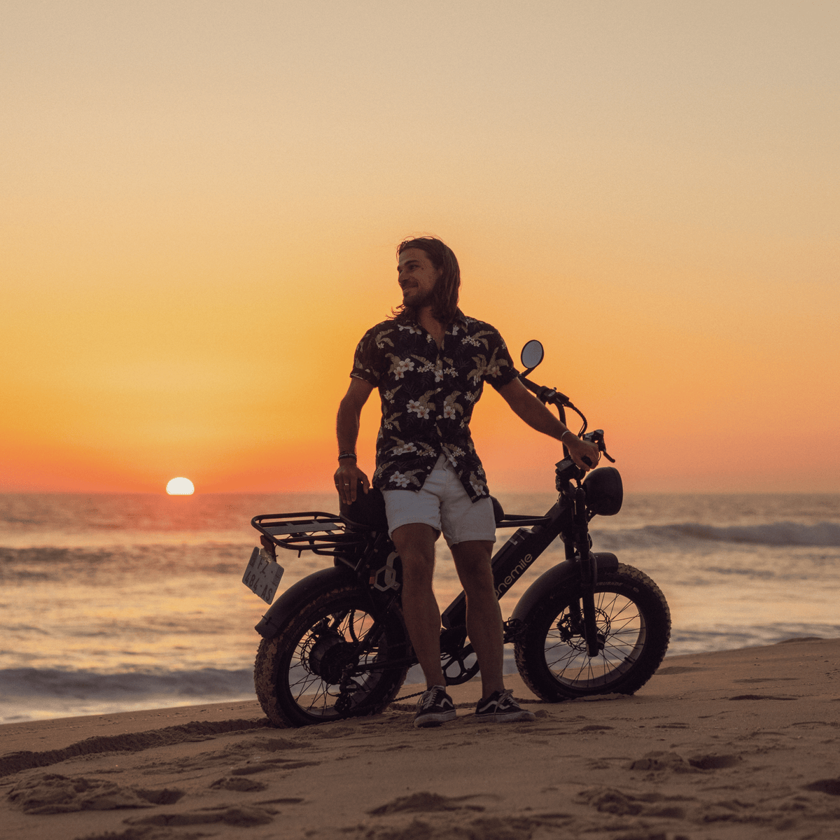 Man står med Onemile P40 Pro fatbike-elcykel vid havet i solnedgång