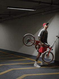 Person står med OneSport OT02 Pro hopfällbar elcykel i färgen röd inomhus