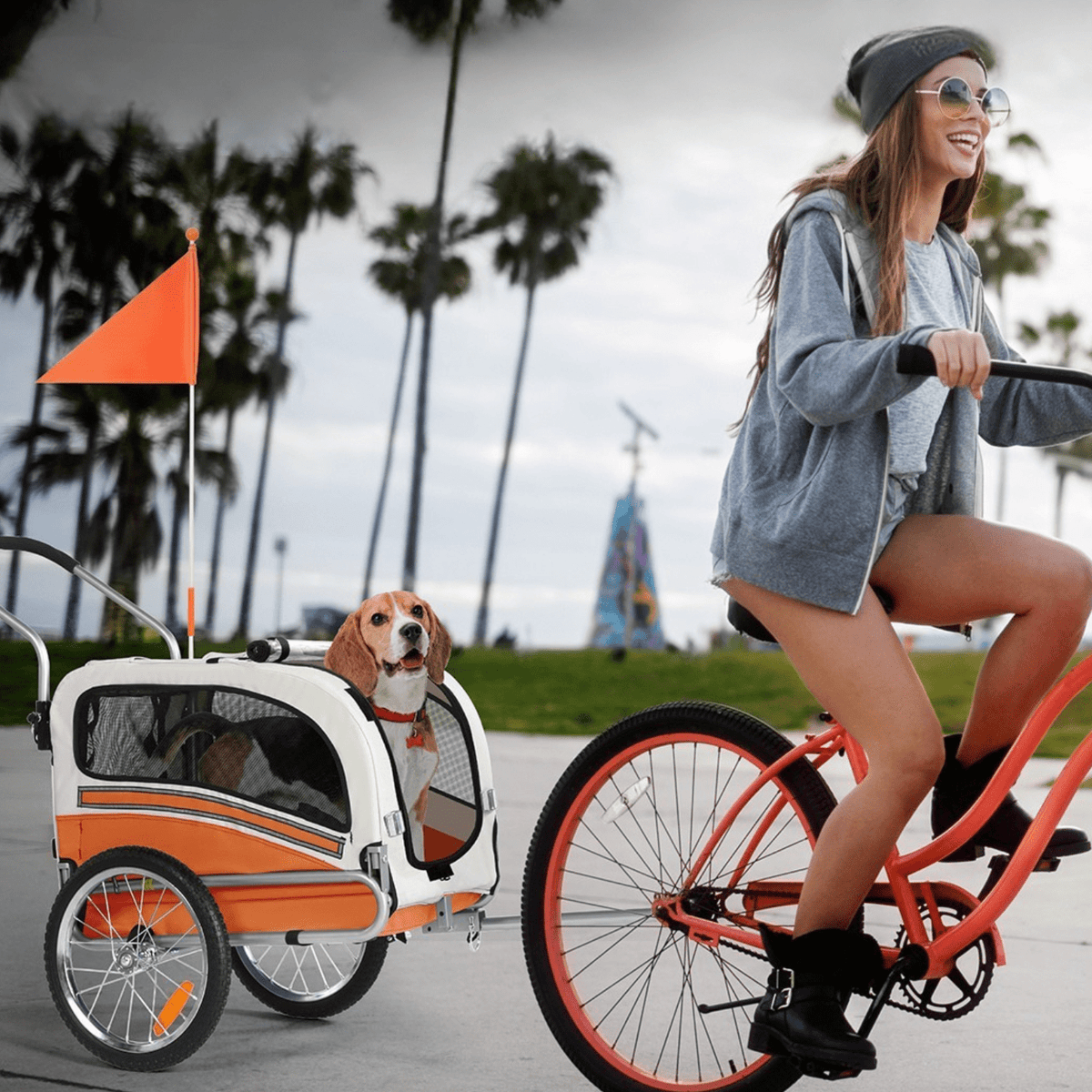 Person som cyklar med Smart 20303B cykelvagn för husdjur i orange på släp med en hund i vagnen bland palmer