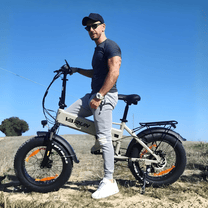 Man står med VARUN S20-1 hopfällbar fatbike-elcykel i färgen beige på en gräsplan