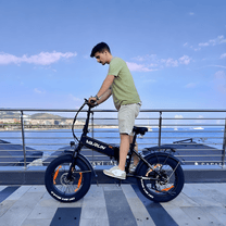Man som kör VARUN S20-1 hopfällbar fatbike-elcykel i färgen svart vid havet