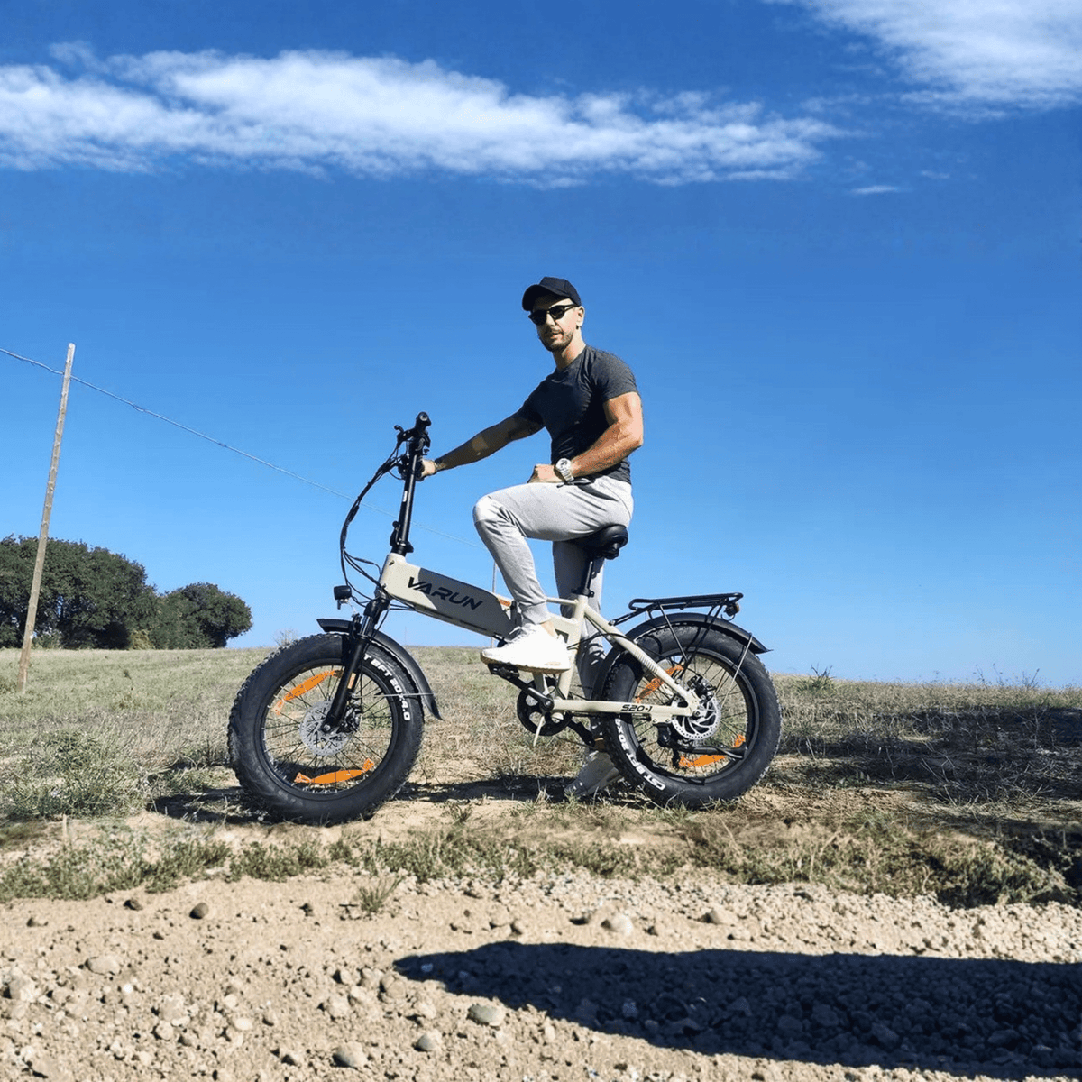 Man som kör VARUN S20-1 hopfällbar fatbike-elcykel i färgen beige på en grusväg