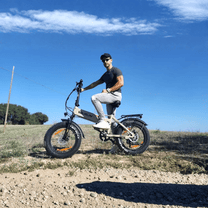 Man som kör VARUN S20-1 hopfällbar fatbike-elcykel i färgen beige på en grusväg