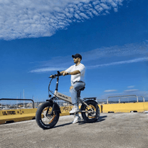 Man som kör VARUN S20-1 hopfällbar fatbike-elcykel i färgen beige vid havet