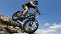 Förare gör ett hopp med VARUN S26-1 fatbike-elcykel med hjälm i bergsmiljö